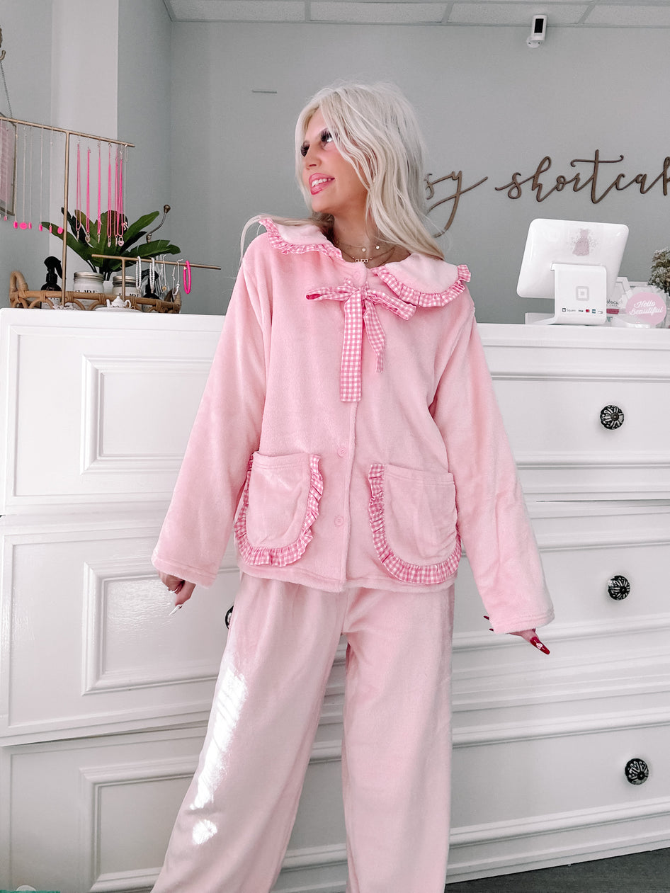 Pink plush pajama set with gingham trim, modeled in a boutique.
