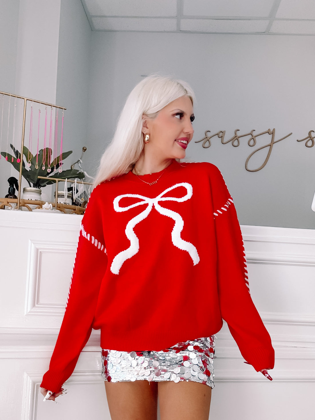 Red sweater featuring a large white bow, styled with a silver sequined skirt.
