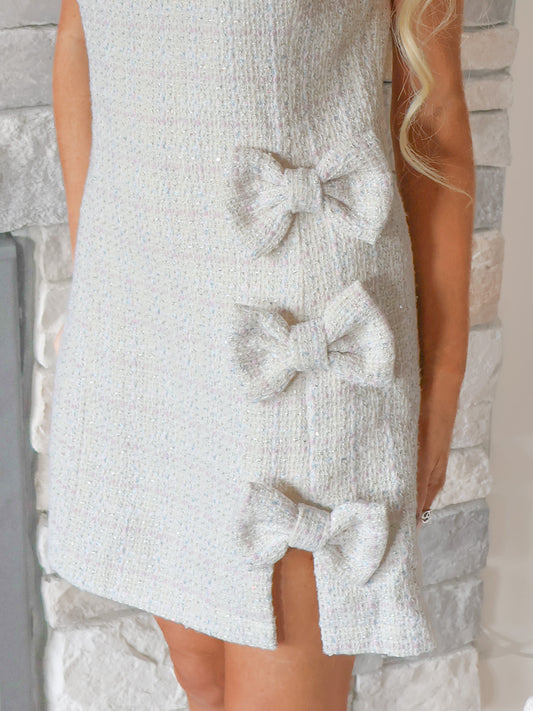 Close-up of Tres Chic Bow Dress by Sassy Shortcake showing white tweed fabric, front slit, and decorative bow details