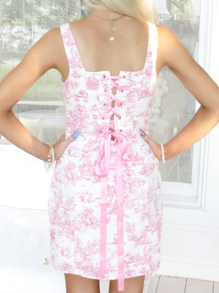 Pink toile print dress with a corset-style back and pink ribbon lacing.
