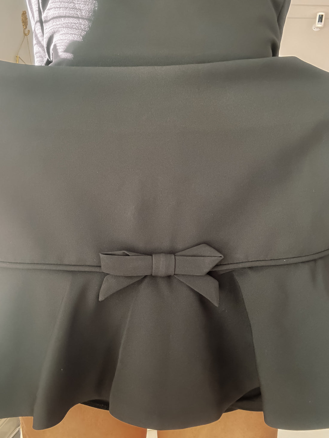 Close-up of black dress detail: a fabric bow adorns the back waistband.
