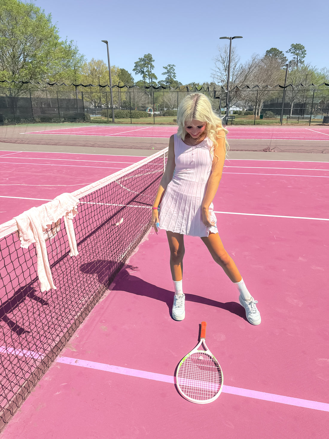 Pink tennis court with a woman in a pleated dress and tennis racket - Pink Twirl & Train ribbed knit dress from Sassy Shortcake
