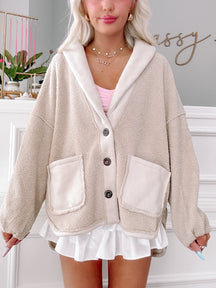 Cream-colored button-front cardigan, featuring a plush texture and contrasting inner lining, shown paired with a white pleated skirt.
