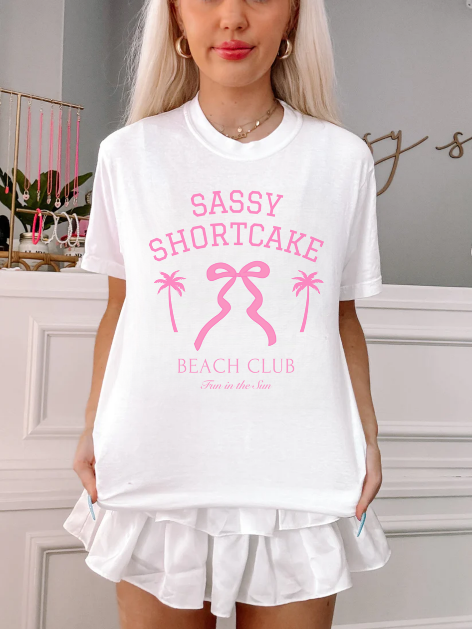 White bow tee styled on model, centered pink bow design in focus.