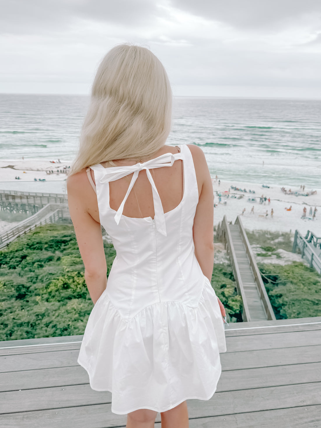 White eyelet summer dress viewed from behind, overlooking ocean beach.

