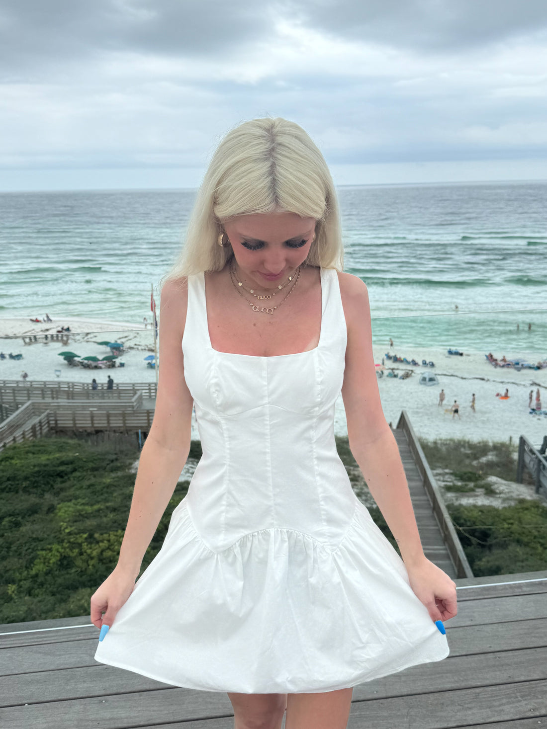 White summer dress with a ruffled hem, worn outdoors near the ocean.
