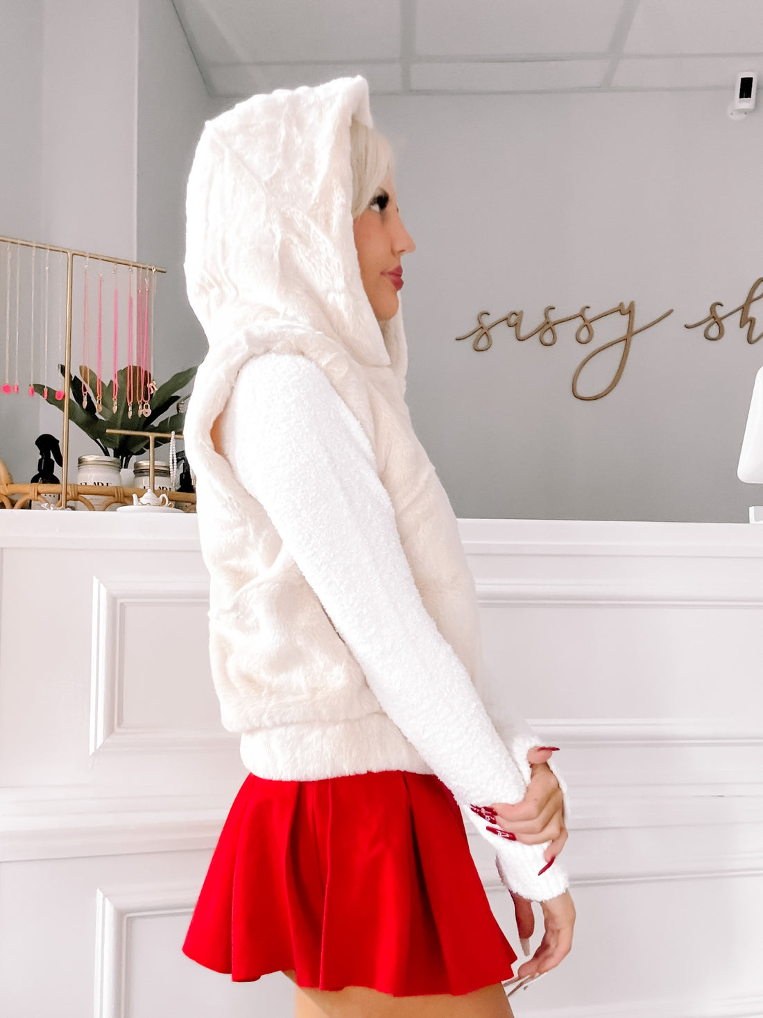 Cream-colored hooded vest, worn with a red skirt, in a bright interior.
