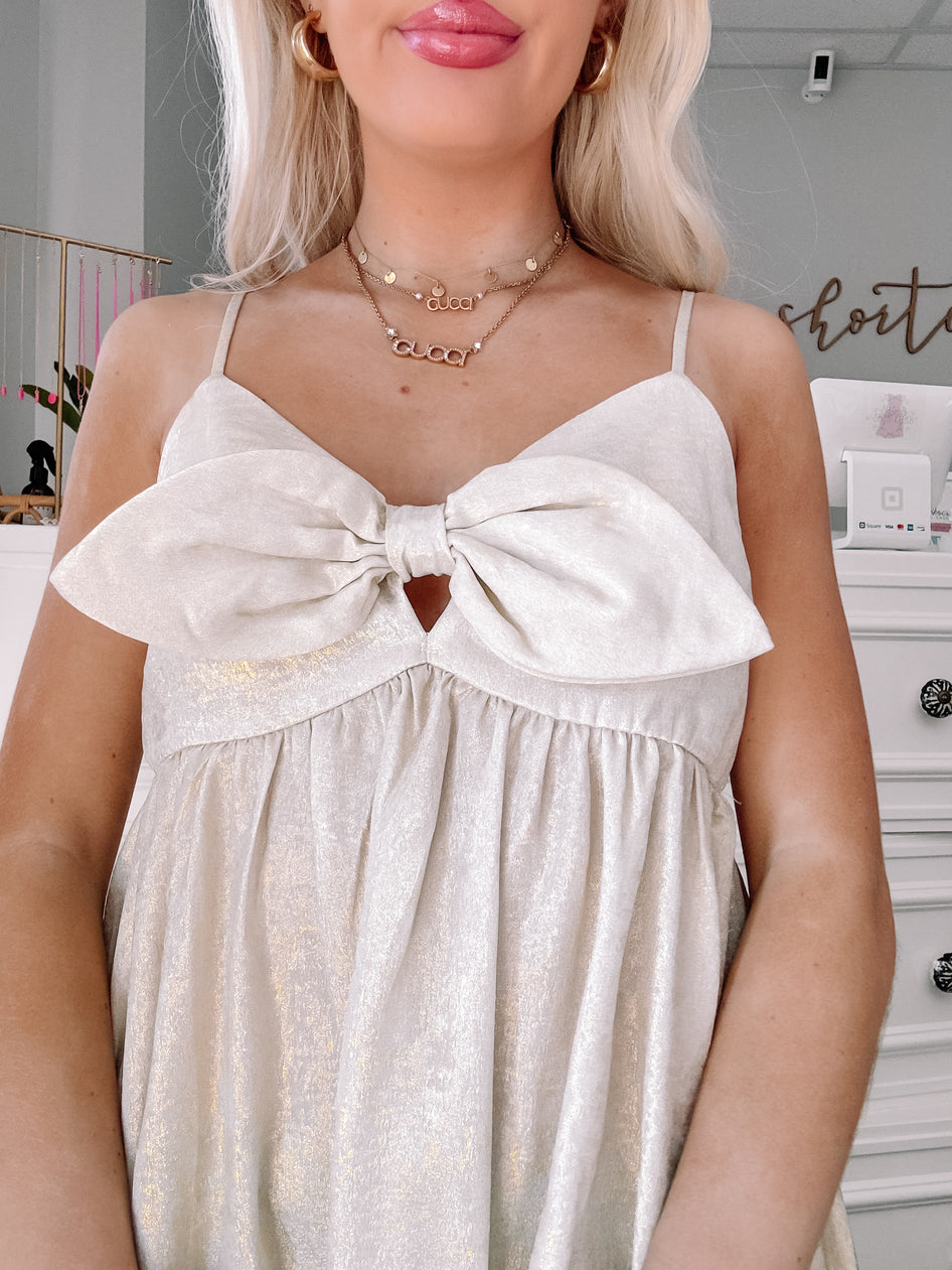 Champagne gold sleeveless dress with a large bow detail at the bust.
