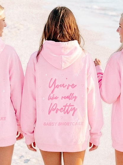 You're Like Really Pretty Hoodie from Sassy Shortcake - Pink hoodie with text on the back worn by a person, with two other people partially visible.
