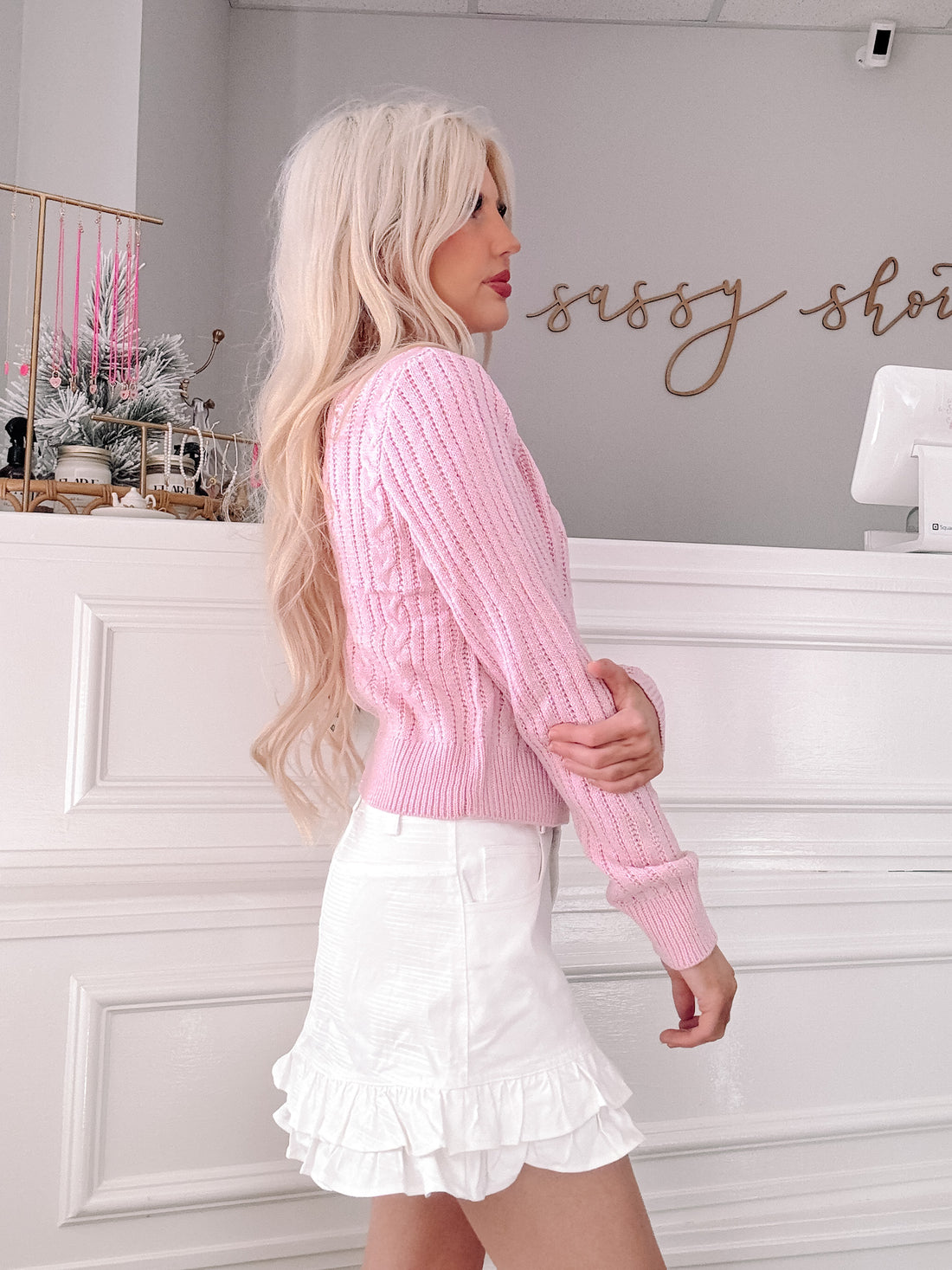Pink cable-knit cropped sweater styled in a boutique setting.
