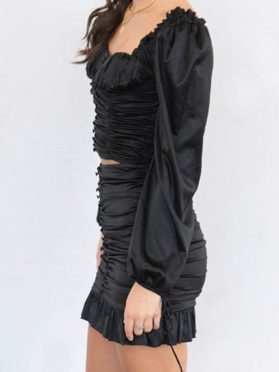 Black satin mini skirt with ruffles and drawstring waist, shown on a model.
