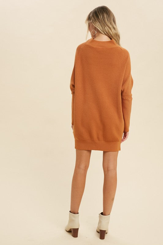 Burnt orange knit tunic sweater dress shown from the back, styled with cream ankle boots.

