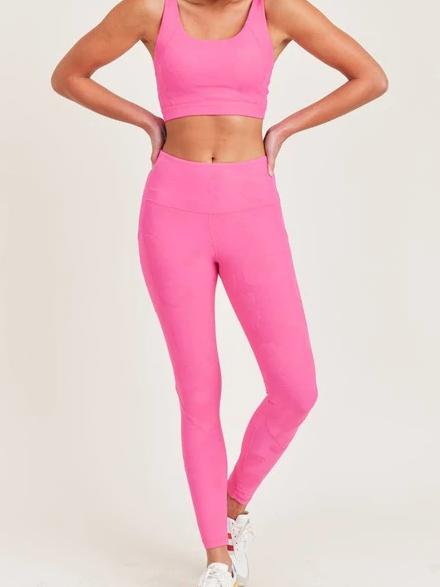Hot pink leggings styled with a matching sports bra, shown on a model.
