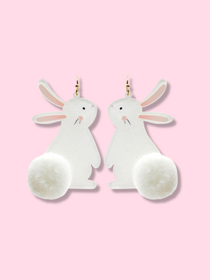 Adorable white bunny earrings with fluffy pom-pom tails, shown against a pink background.

