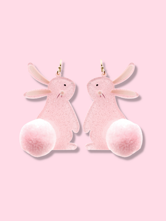 Pink bunny rabbit dangle earrings with fluffy pom-pom tails, shown against a light pink background.

