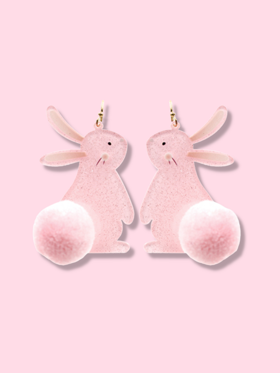 Pink bunny rabbit dangle earrings with fluffy pom-pom tails, shown against a light pink background.
