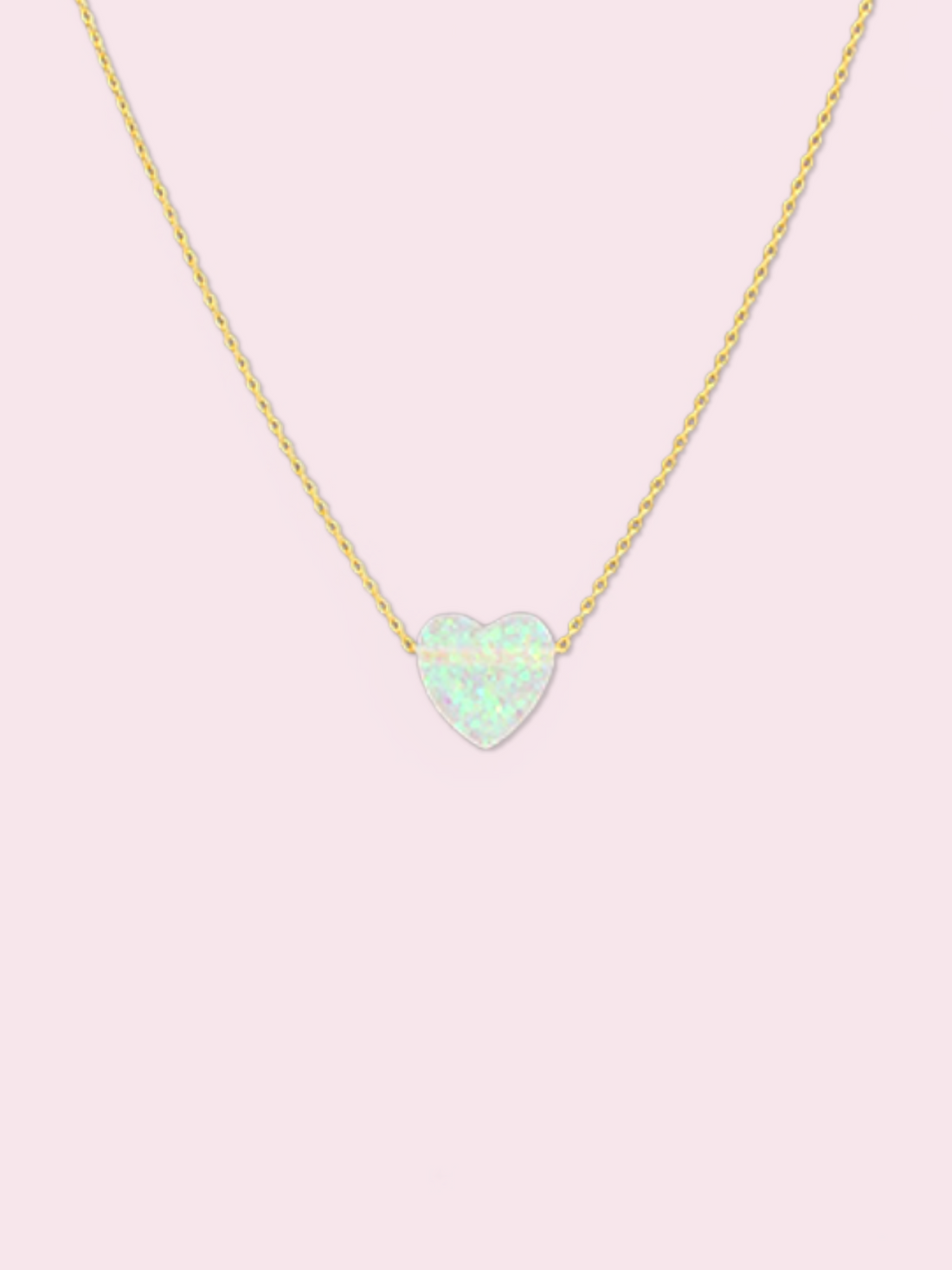 Dainty gold chain necklace featuring a pale opal heart pendant against a light pink backdrop.

