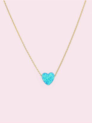 Dainty gold chain necklace featuring a light blue opal heart pendant against a pale pink background.
