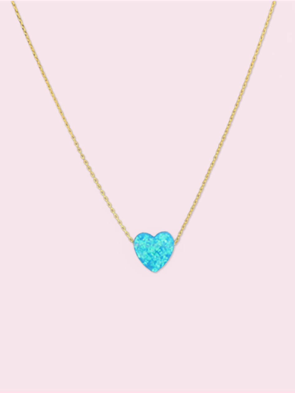 Dainty gold chain necklace featuring a light blue opal heart pendant against a pale pink background.
