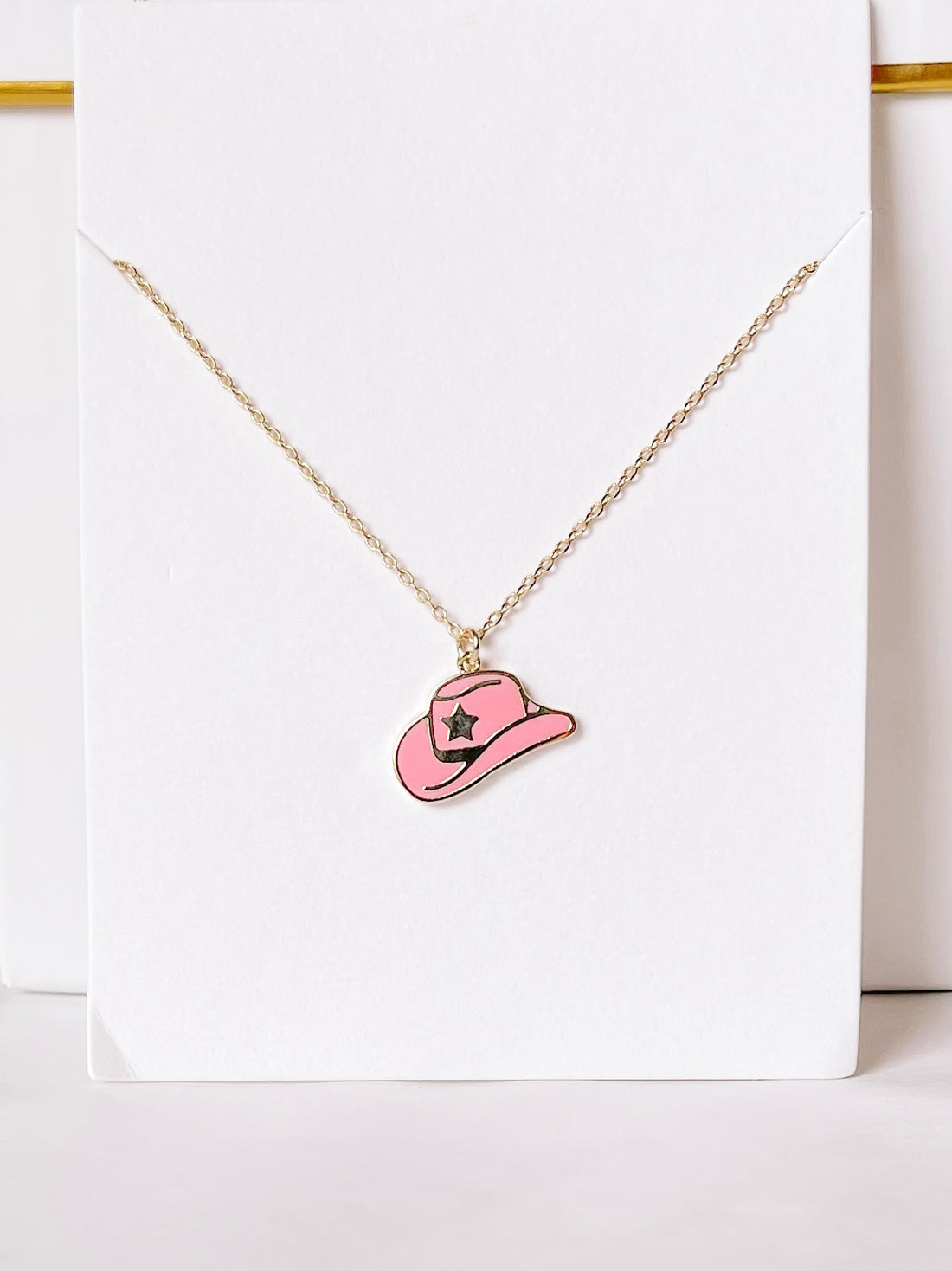 Gold chain necklace featuring a pink cowboy hat charm.
