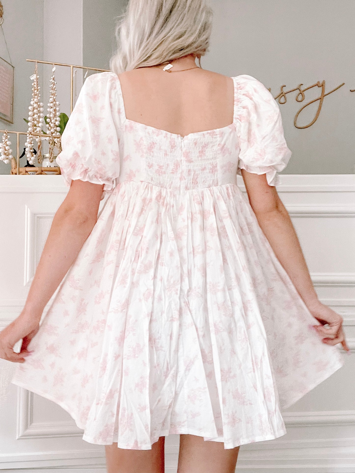 Pink floral mini dress with puff sleeves, shown from the back against a white wall.
