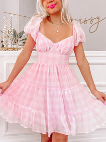Pink gingham mini dress with puff sleeves and tiered skirt, styled at home.
