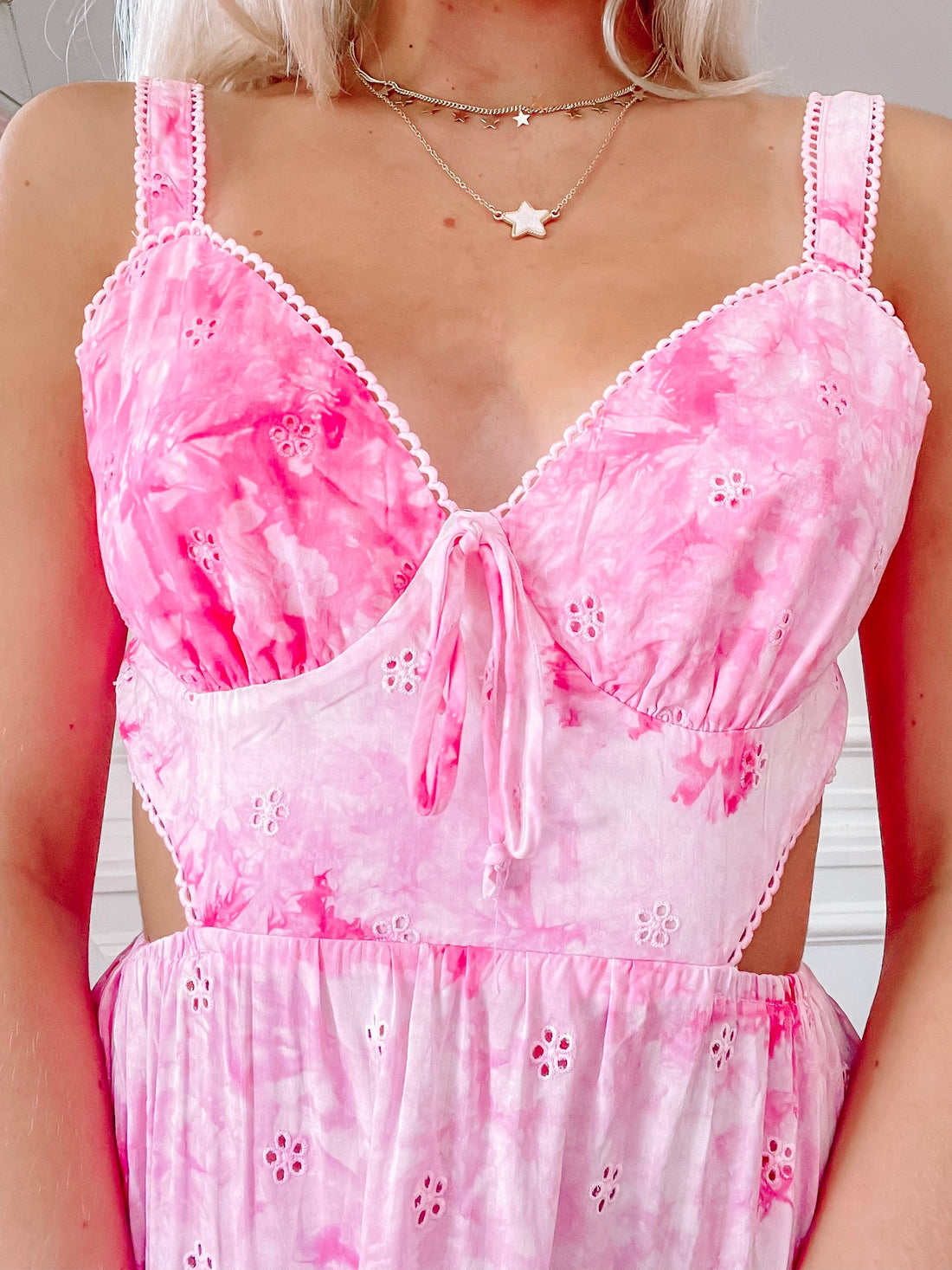 Pink tie-dye eyelet dress with cutout sides and a ruffled hem.
