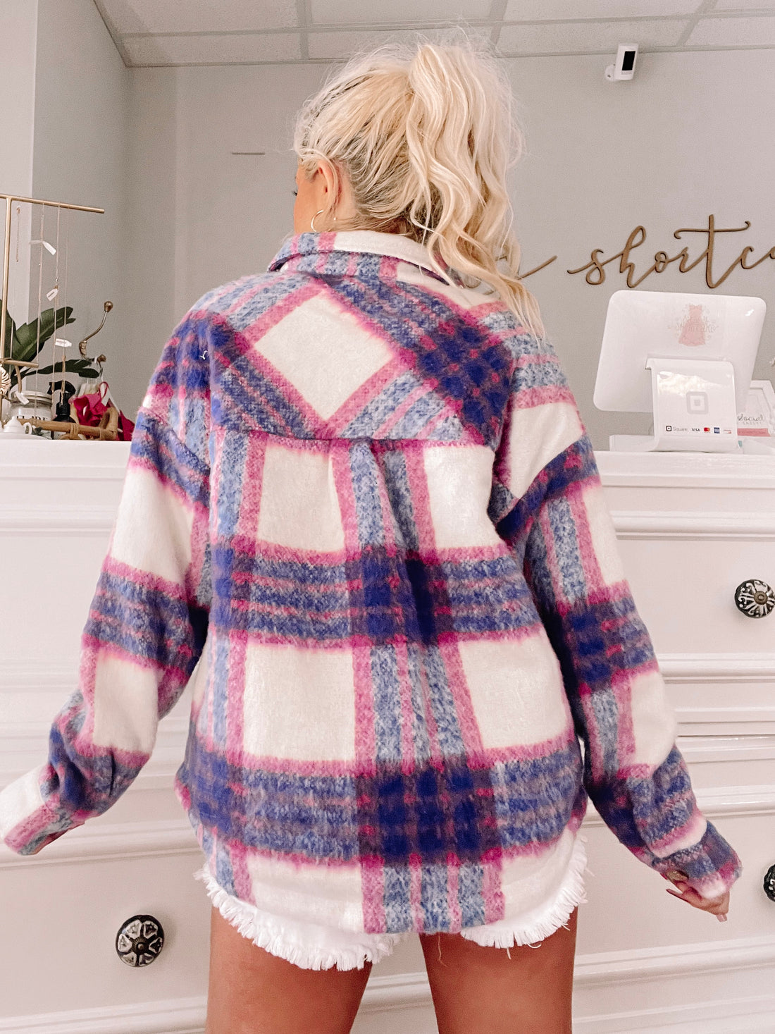 Cozy pink, purple, and white plaid shacket shown from the back in a shop setting.

