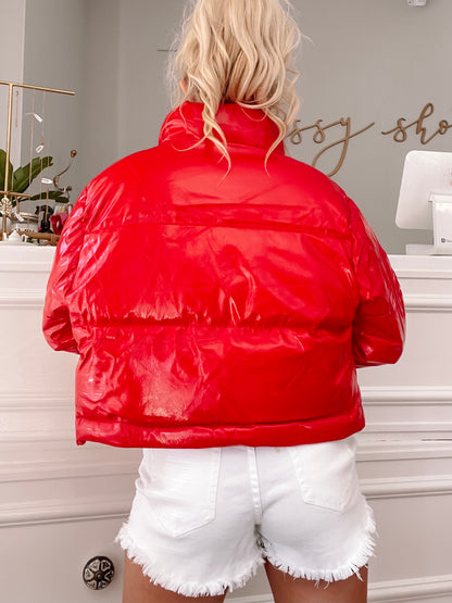 Shiny red puffer jacket, cropped view showcasing the back, in a bright shop setting.
