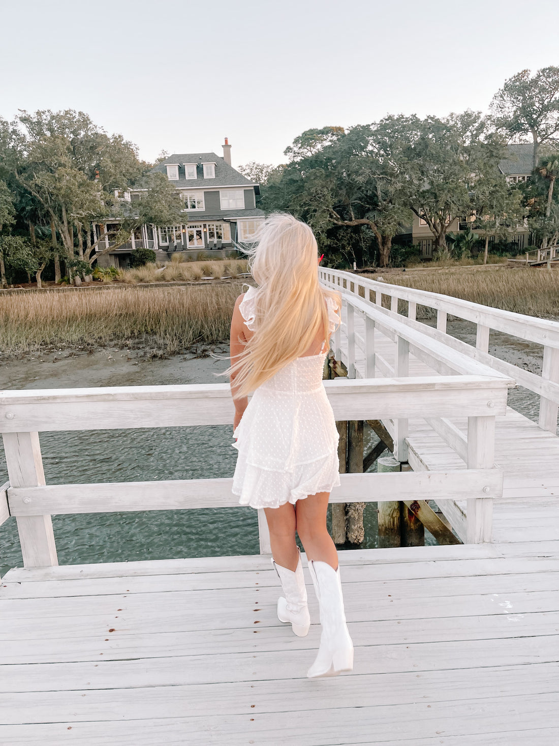 White eyelet dress and white cowboy boots on a waterfront dock.
