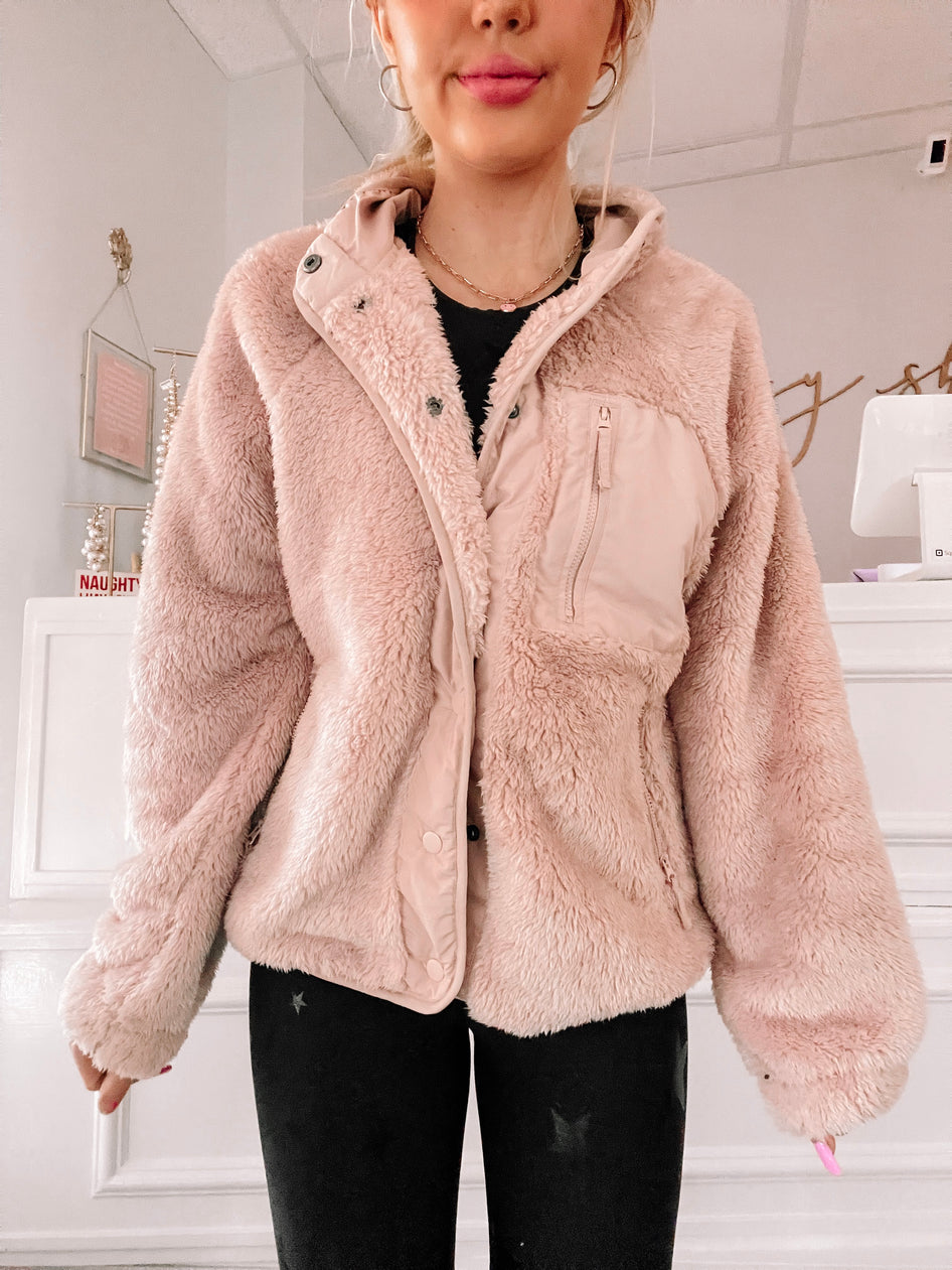 Blush pink fluffy fleece jacket, button and zipper closure, worn indoors against a white wall.
