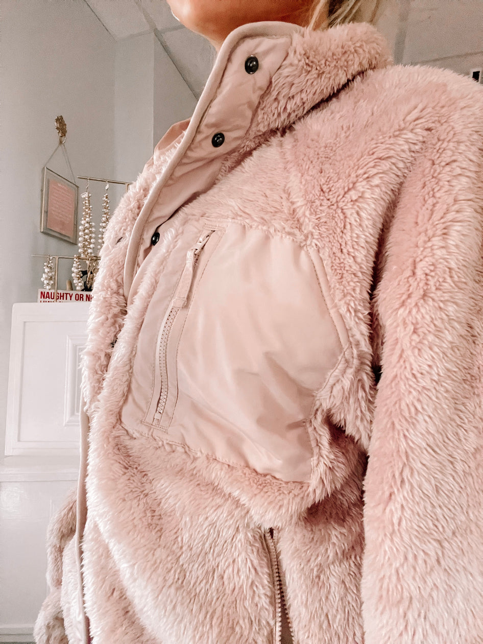 Soft blush pink plush jacket, featuring a zipper and snap closures, shown in a home setting.
