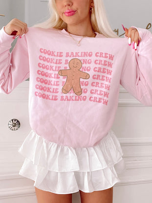 Pink gingerbread man crewneck sweatshirt with repeated "Cookie Baking Crew" text.
