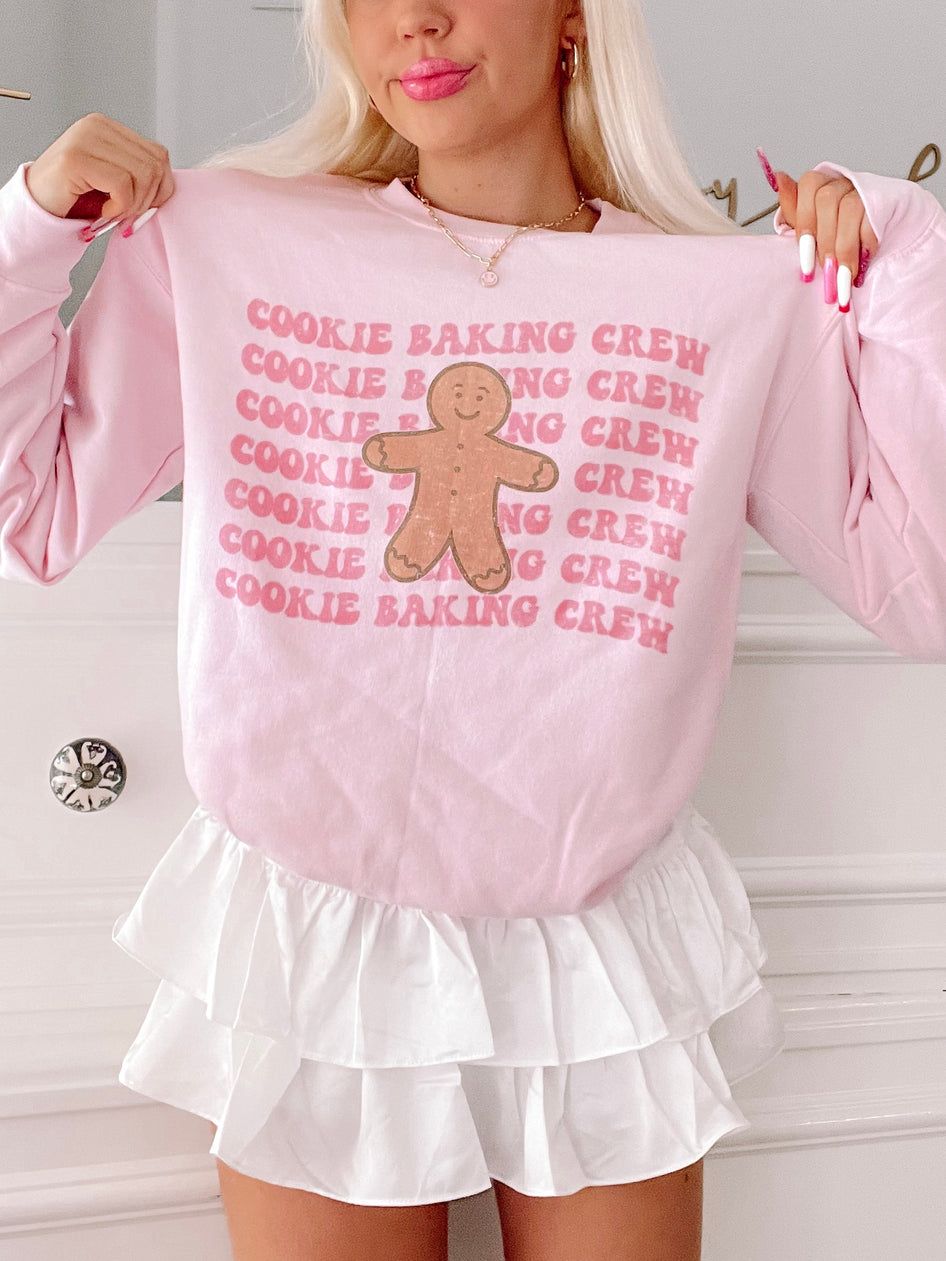 Pink gingerbread man crewneck sweatshirt with repeated "Cookie Baking Crew" text.
