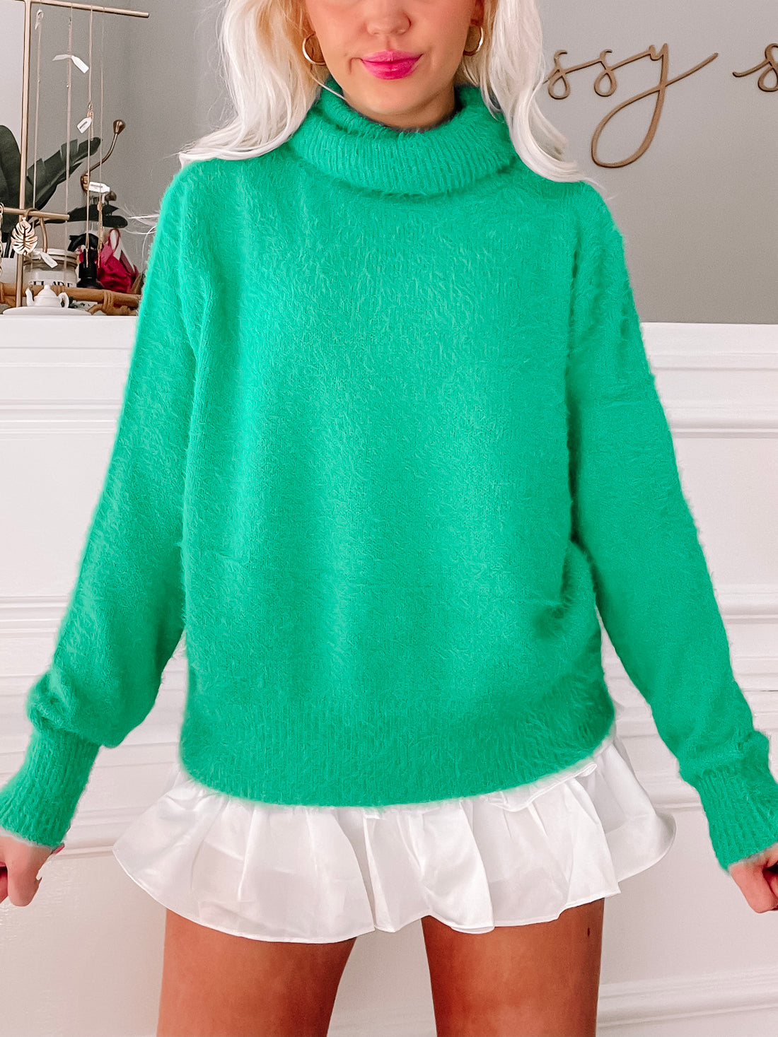 Fuzzy green turtleneck sweater with long sleeves, styled with a white ruffled skirt.
