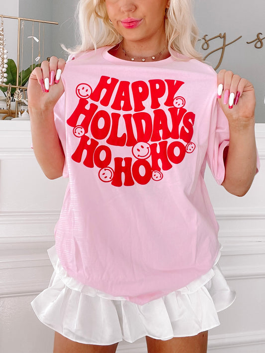 Pink holiday tee with red "Happy Holidays Ho Ho Ho" graphic and smiling faces.