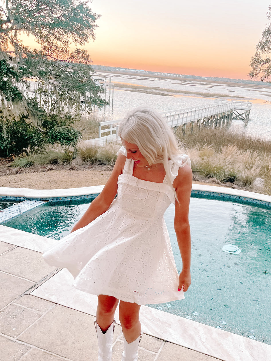 White eyelet dress twirled near a pool at sunset.
