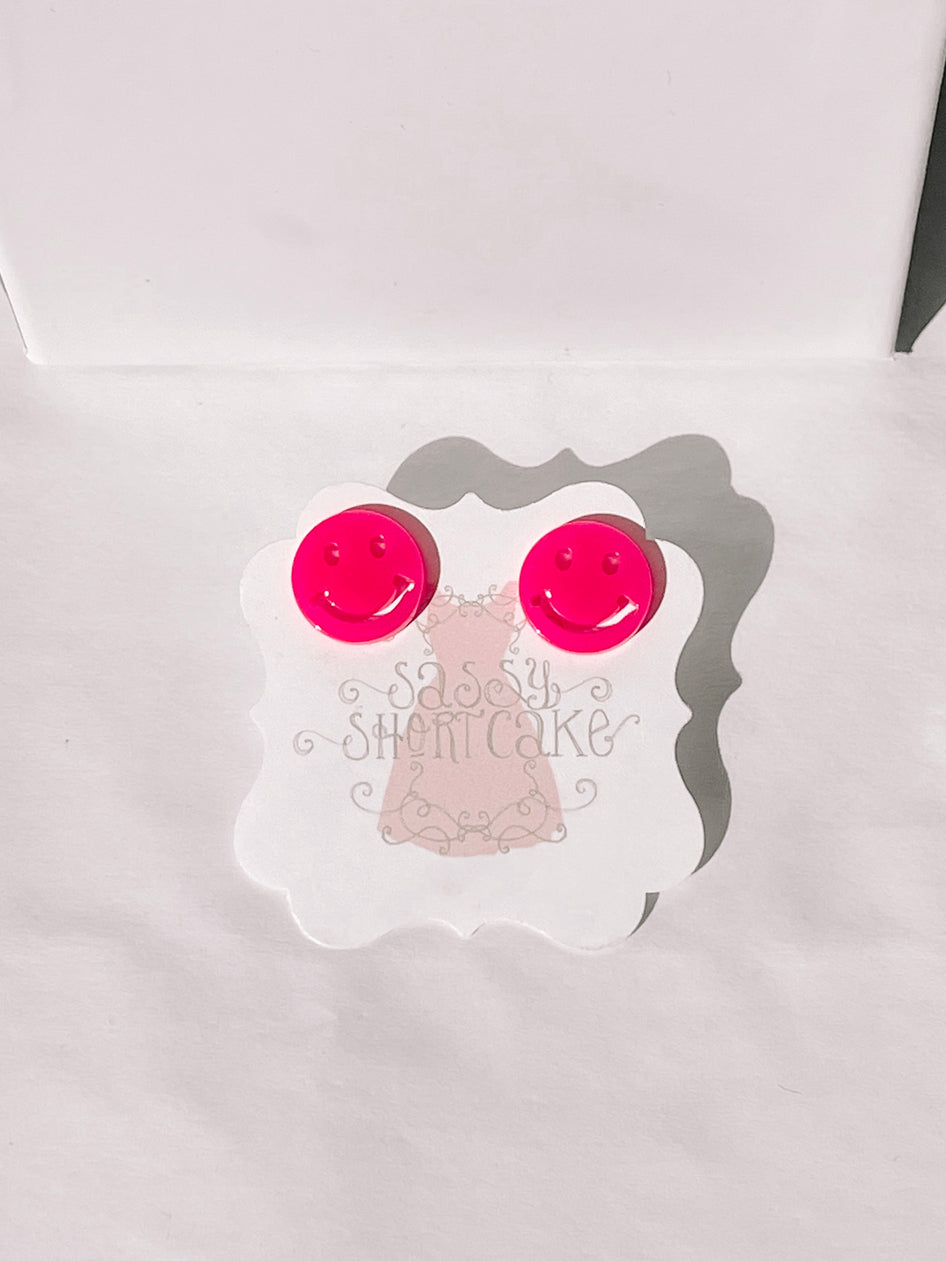 Bright pink smiley face earrings displayed on a white card.
