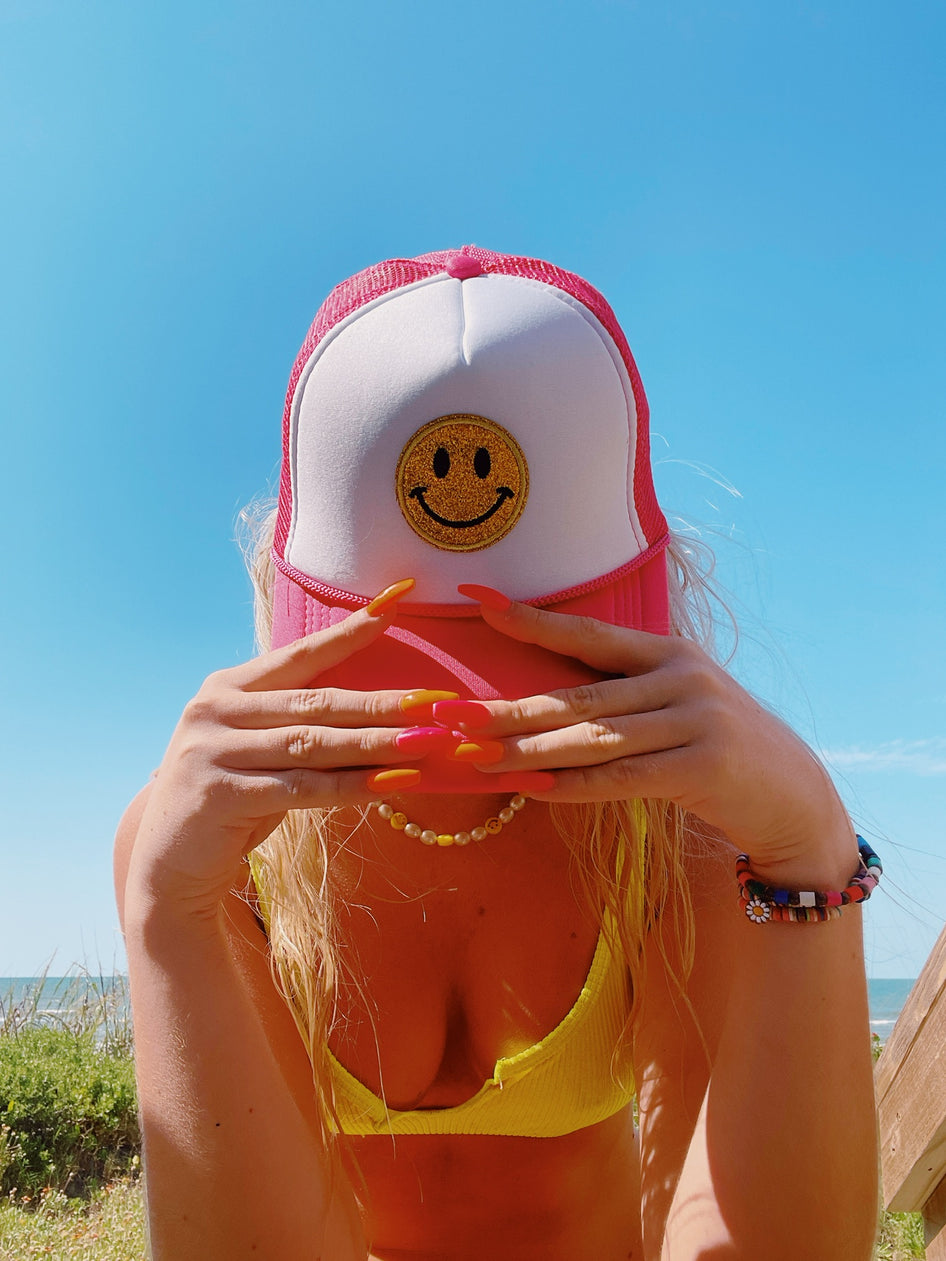 Pink and white trucker hat with glitter smiley face, perfect for summer.
