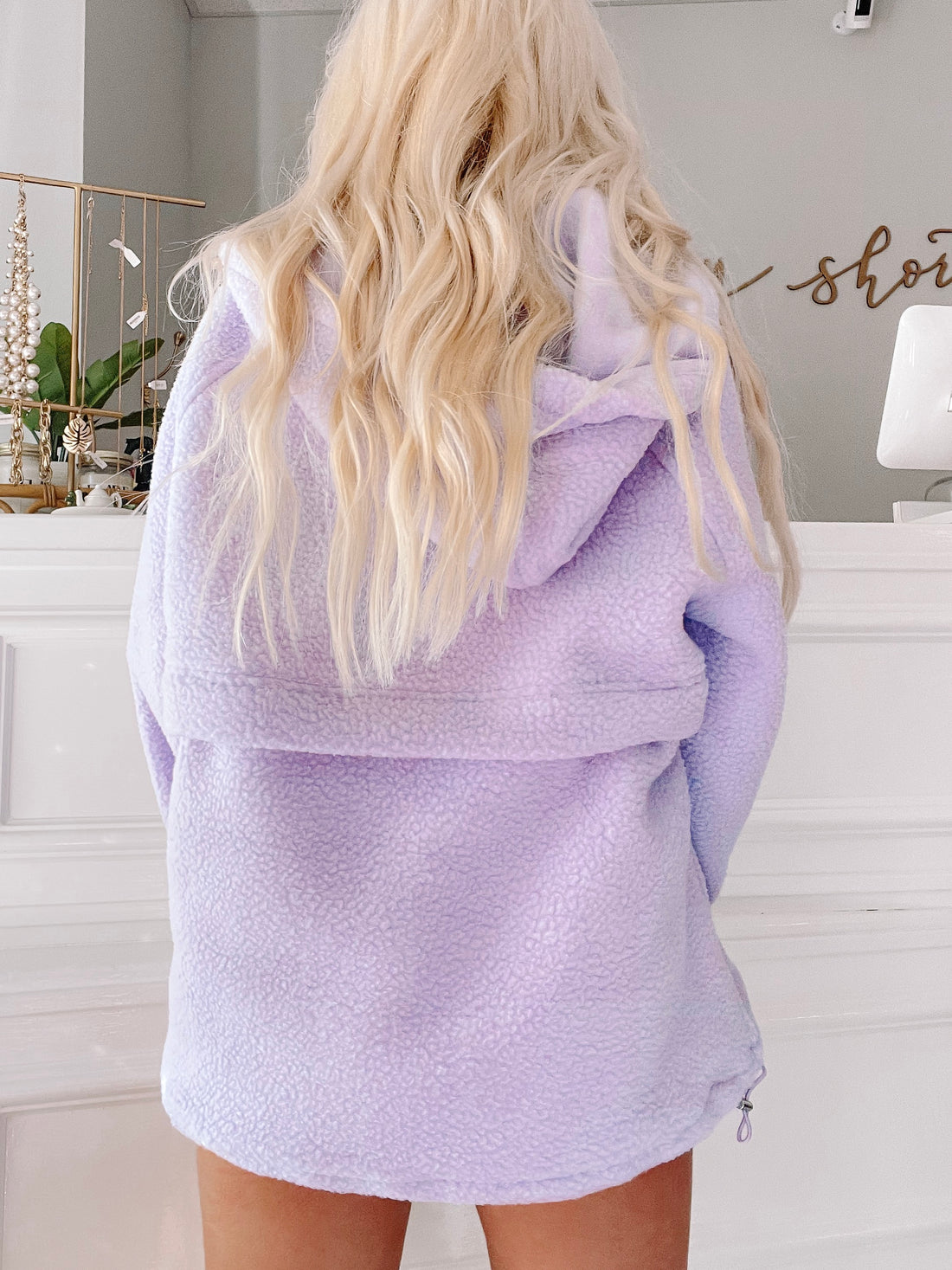 Lavender-colored fleece pullover with a hood, shown from the back in a shop setting.
