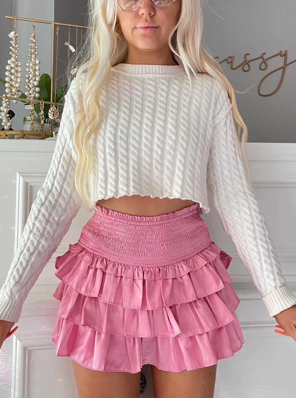 Pink tiered ruffle mini skirt with elastic waistband, styled with a cream cable knit sweater.
