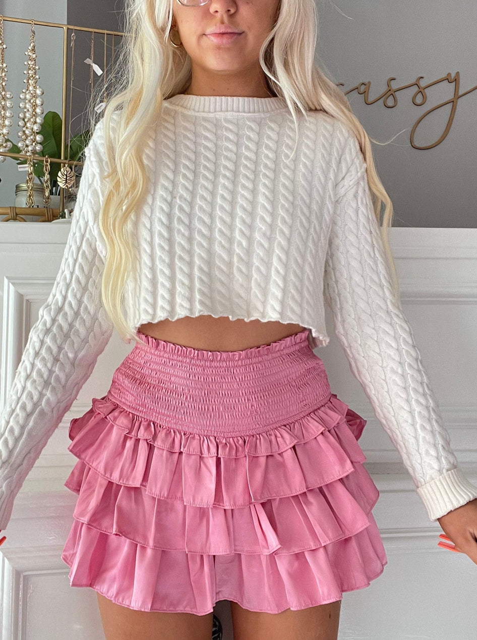 Dusty rose ruffled mini skirt with elastic waistband, modeled with a cream cable knit sweater.

