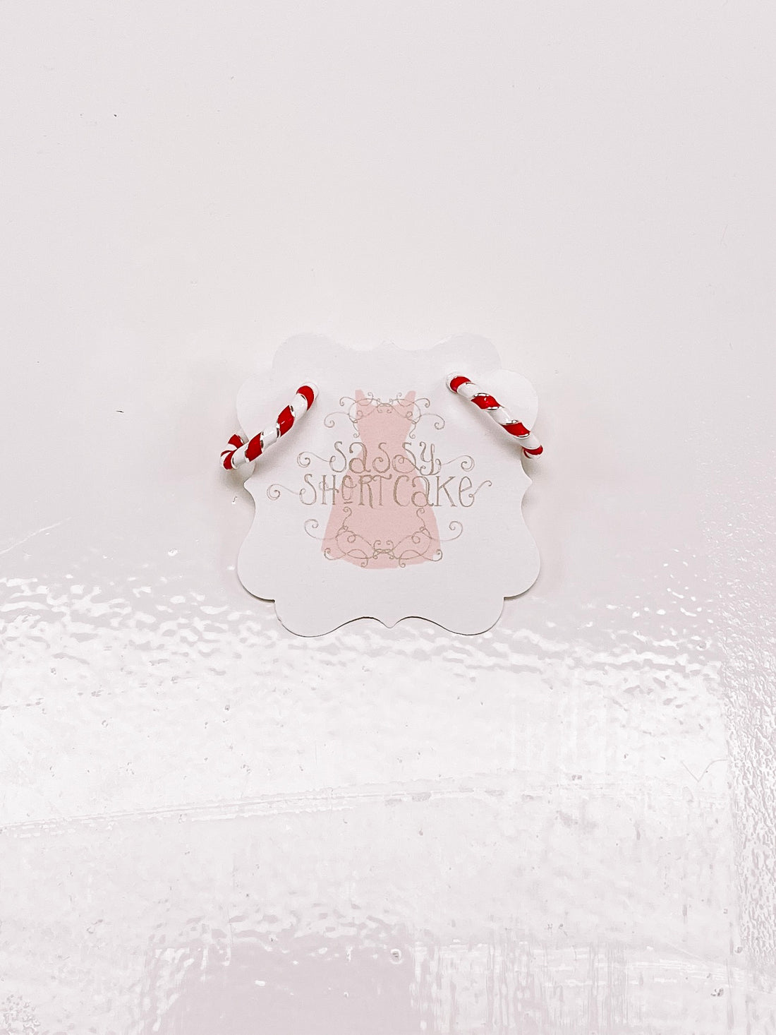 Candy cane-striped hoop earrings displayed on a product tag against a white background.

