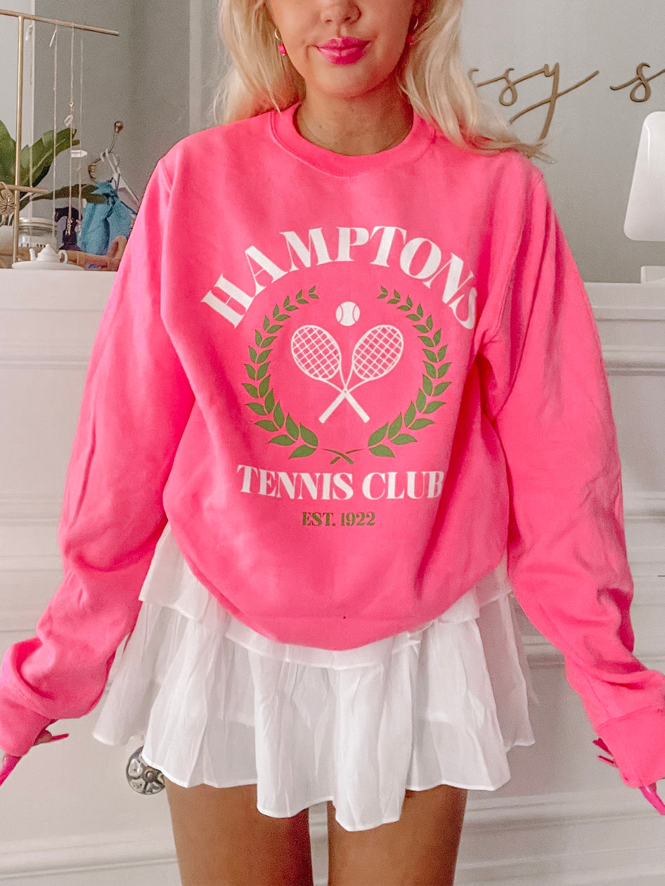 Bright pink crewneck sweatshirt featuring a tennis club graphic;  model shown wearing with white pleated skirt.
