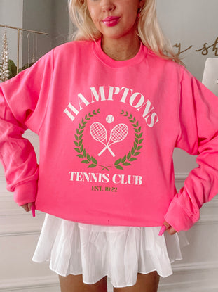Hot pink crewneck sweatshirt featuring a tennis club graphic;  model wears with white pleated skirt.
