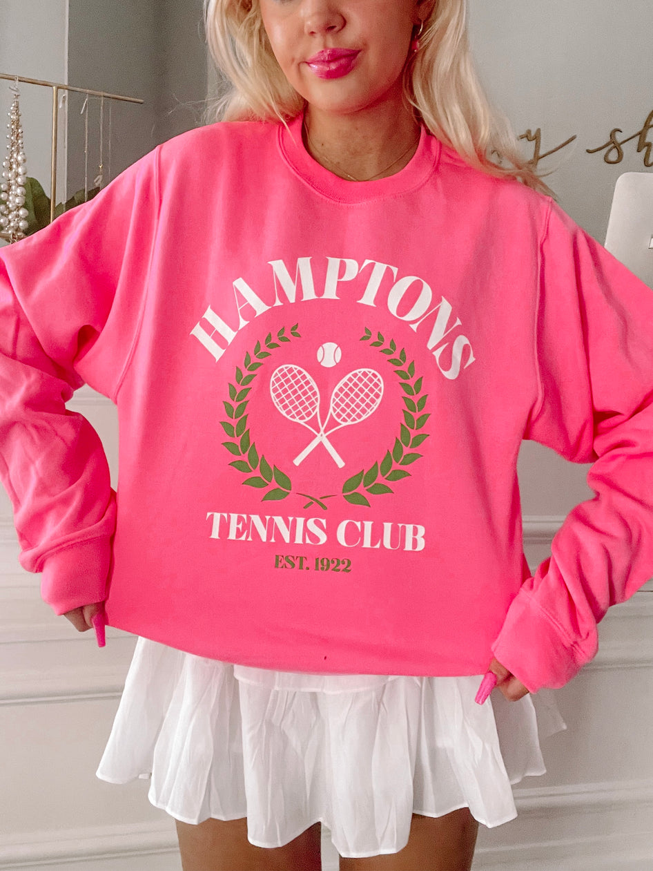 Hot pink crewneck sweatshirt featuring a tennis club graphic;  model wears with white pleated skirt.
