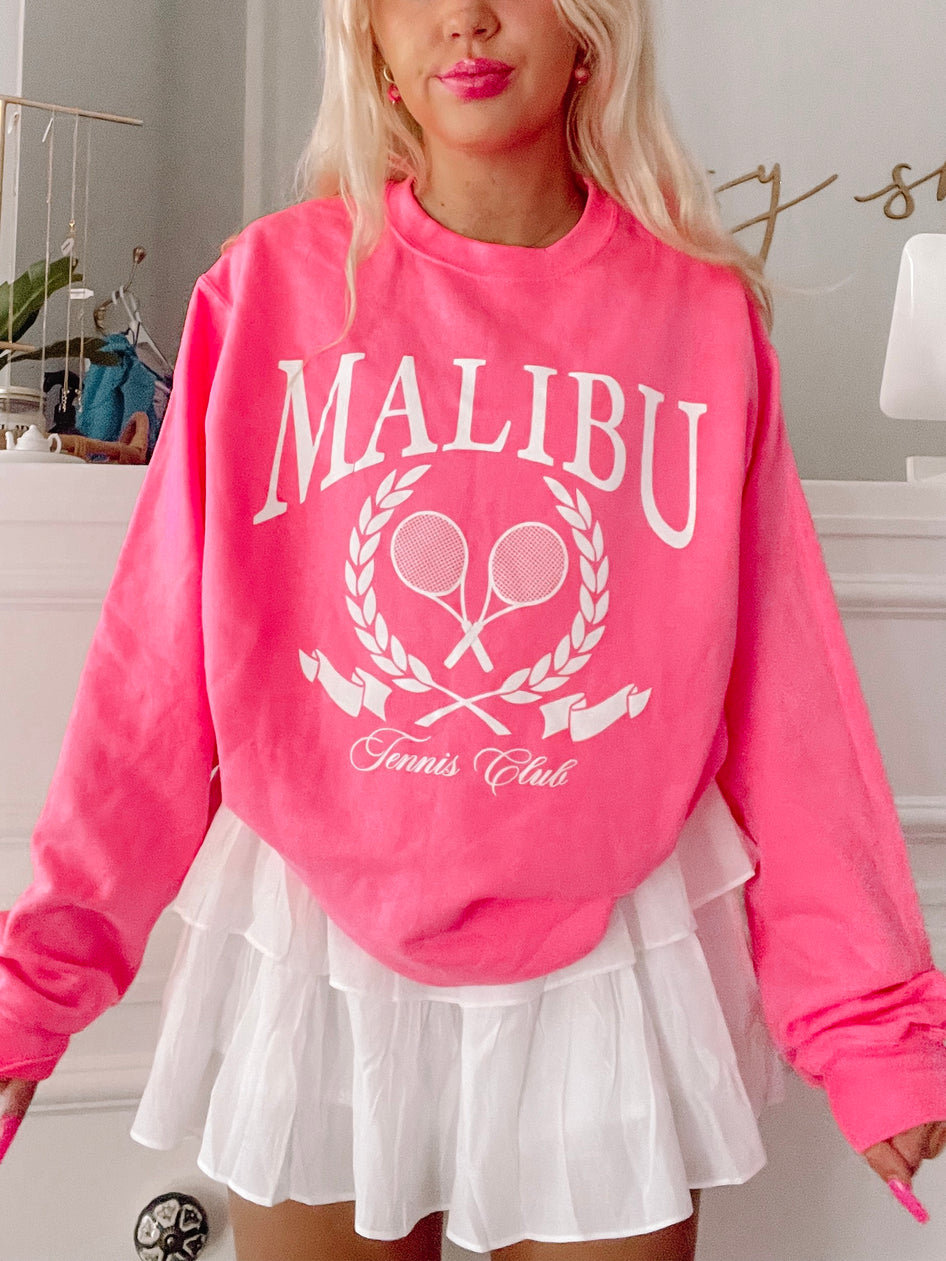 Hot pink crewneck sweatshirt with tennis club graphic;  model wears white ruffled skirt.
