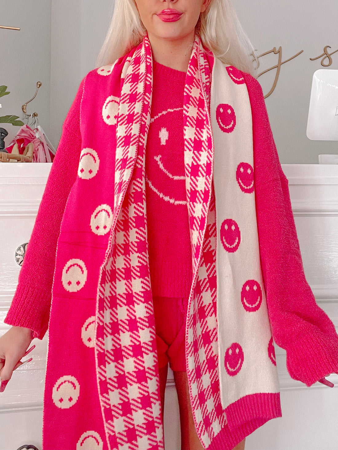 Hot pink and cream knit scarf featuring a cheerful smiley face pattern and houndstooth trim.
