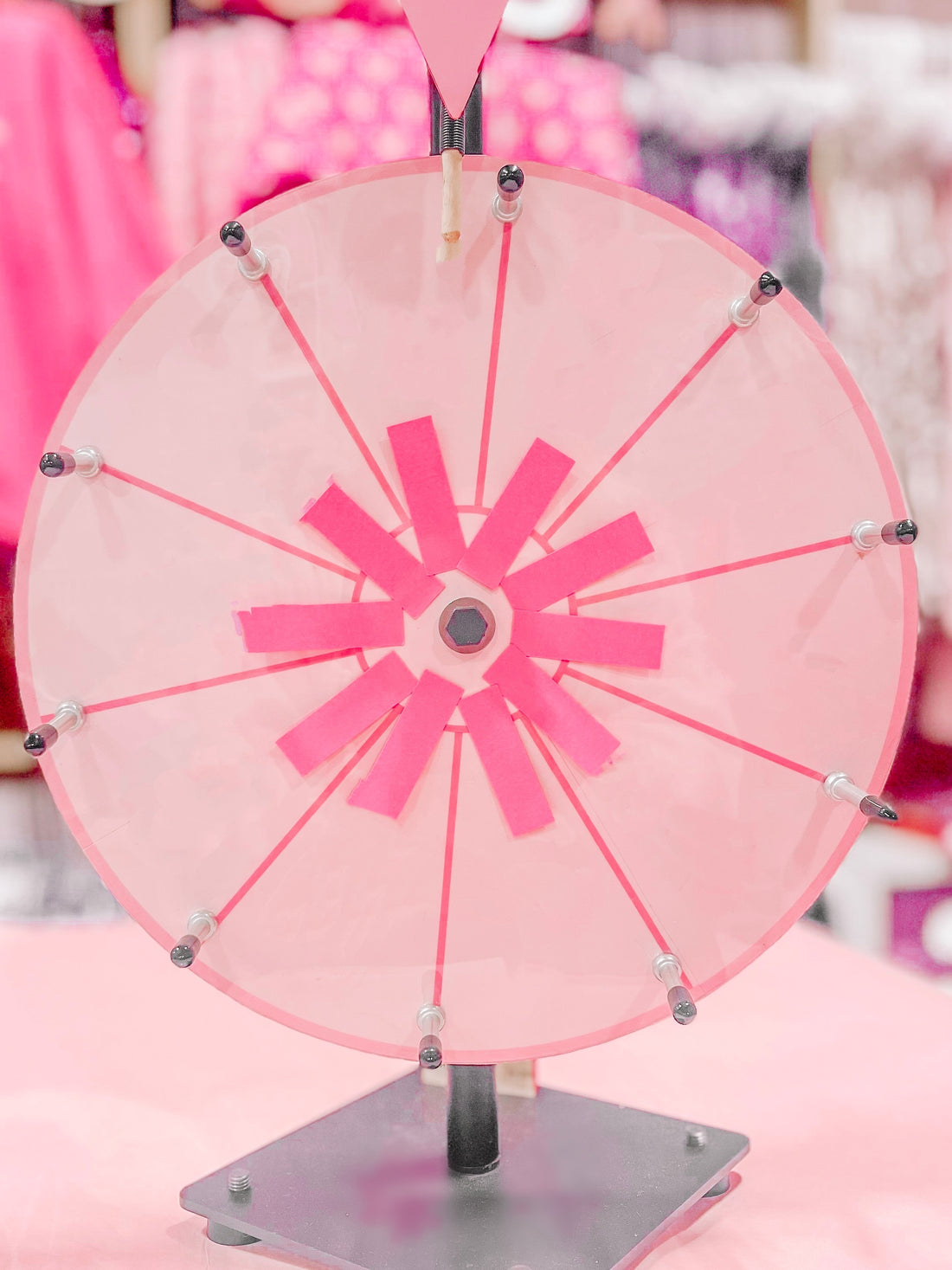 Pink spinning prize wheel with pink paper sections, on a pink surface.
