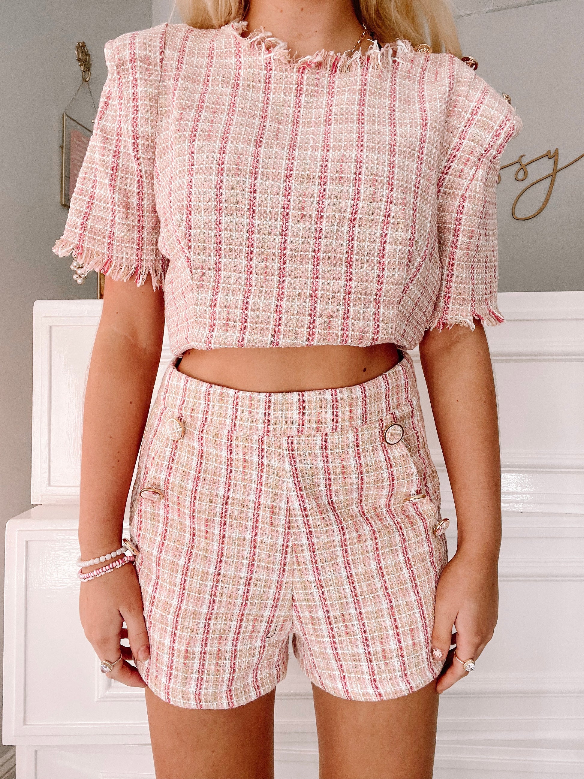 Pink and beige tweed shorts with gold buttons, shown on a model.
